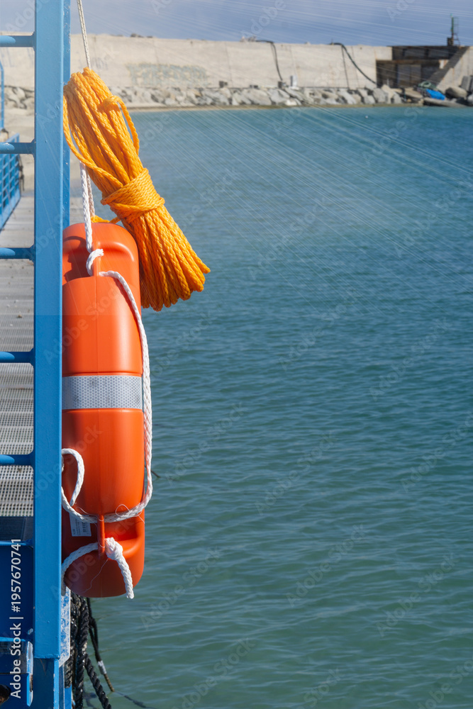 Fototapeta premium lifebuoy rescue ring orange plastic safety equipment on blue pier with copy space for banner design yellow rope and sea water background concept of maritime, safety, tourism