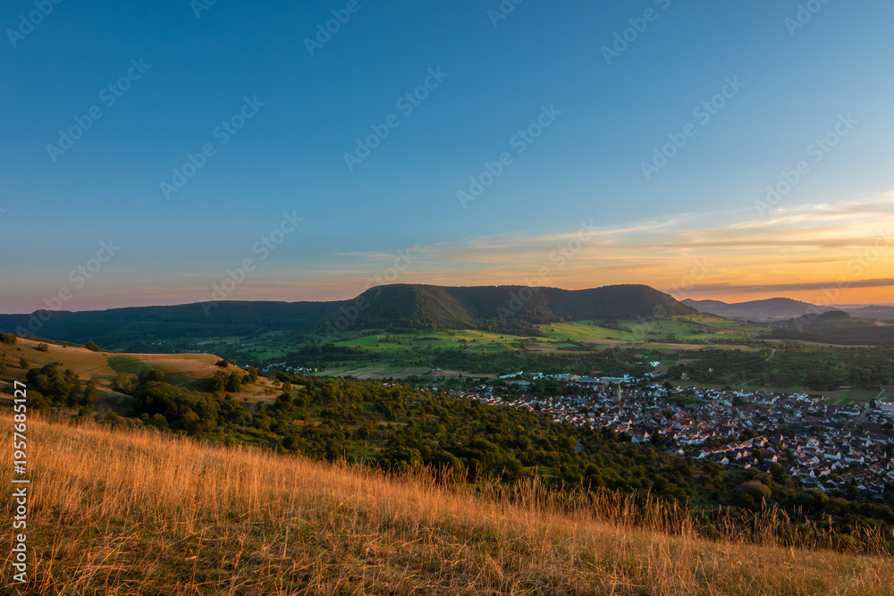 Fototapeta premium Panoramic Sunset Over a Rural Village Nestled in a Lush Green Valley with Rolling Hills in the swabian alb