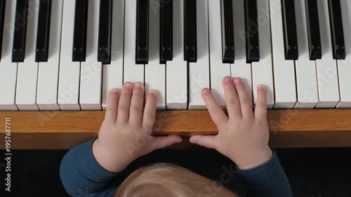 Baby hands on piano keys playing simple tones, top view of infant practicing on wooden keyboard in cozy home setting, natural light, focus on finger coordination, discovery and early learning joy