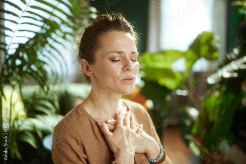 Obraz na płótnie A woman focuses on deep, restorative breaths with her hands on her chest, cultivating inner peace and nervous system regulation in a serene, natural indoor setting