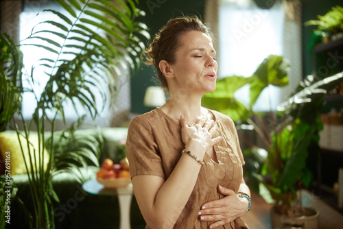 A woman practices deep, diaphragmatic breathing with her hands on her chest and stomach, fostering inner peace and stress relief in her comfortable living room.