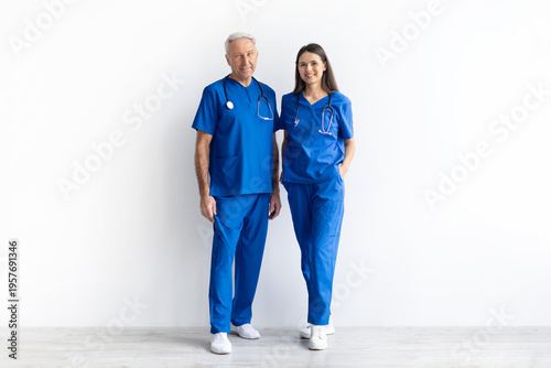 Photos Full length portrait of two healthcare professionals in blue scrubs standing on a white studio background