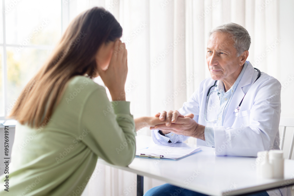 Obraz premium Senior male doctor comforting emotional female patient during medical consultation. Healthcare professional offering empathy and psychological support