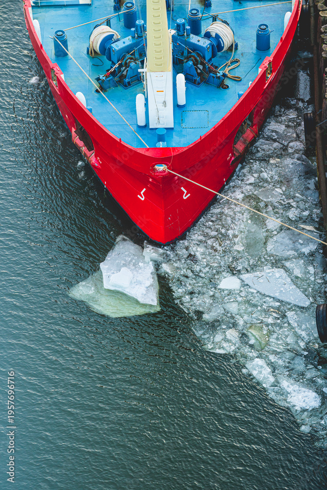 Fototapeta premium Red ship bow docked in icy harbor during cold winter evening.