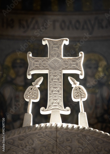 A beautiful carved white marble Greek cross against a backdrop of mosaic icons