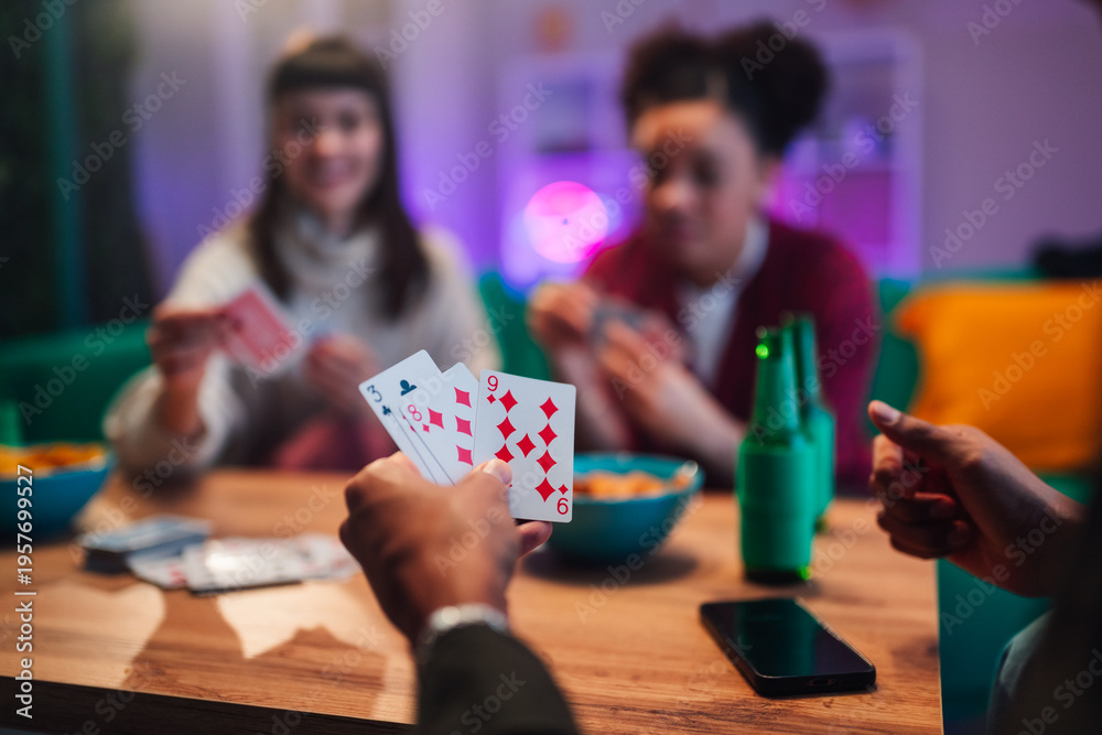 Fototapeta premium Diverse friends playing cards at a table with snacks and drinks, sharing laughter and bonding during a relaxed evening