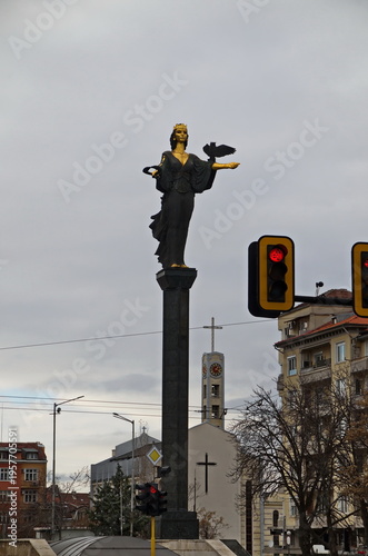 Beautiful corner with golden statue of Saint Sophia, symbol of wisdom and protector of the city, traffic lights with red light and clock tower with cross, Sofia, Bulgaria 