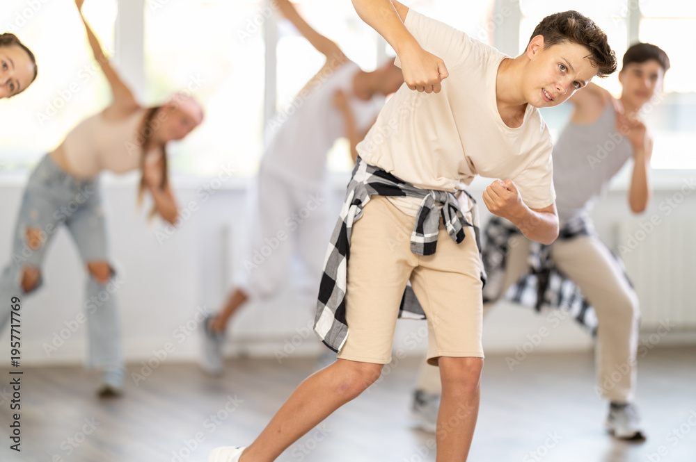 Fototapeta premium Dynamic teenage boy training hip hop slides in dancehall during workout session in group
