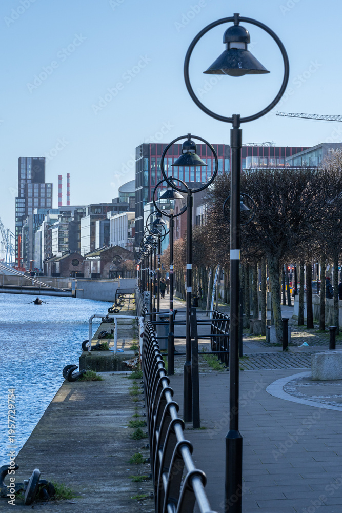Naklejka premium Street lamps line riverwalk beside Dublin skyline