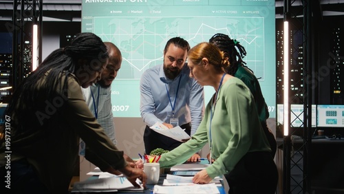 Diverse group of professionals review files and performance metrics, using projections and budgeting to align the company goals with stakeholder expectations for company progress. Camera A.