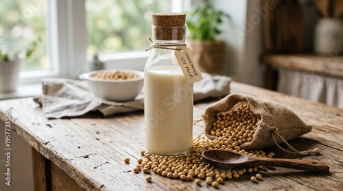 A glass bottle filled with creamy soy milk stands on a rustic wooden table surrounded by dried soybeans spilling from a small burlap sack next to a wooden spoon