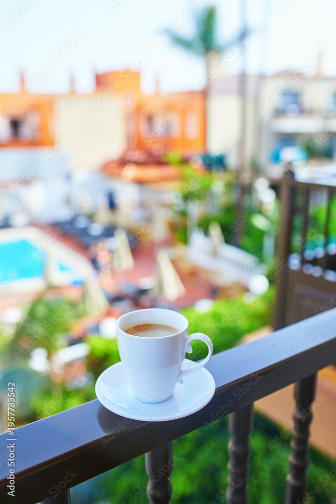Obraz premium Cup of coffee on a hotel balcony overlooking a swimming pool and tropical courtyard in Tenerife, Canary Islands, Spain.