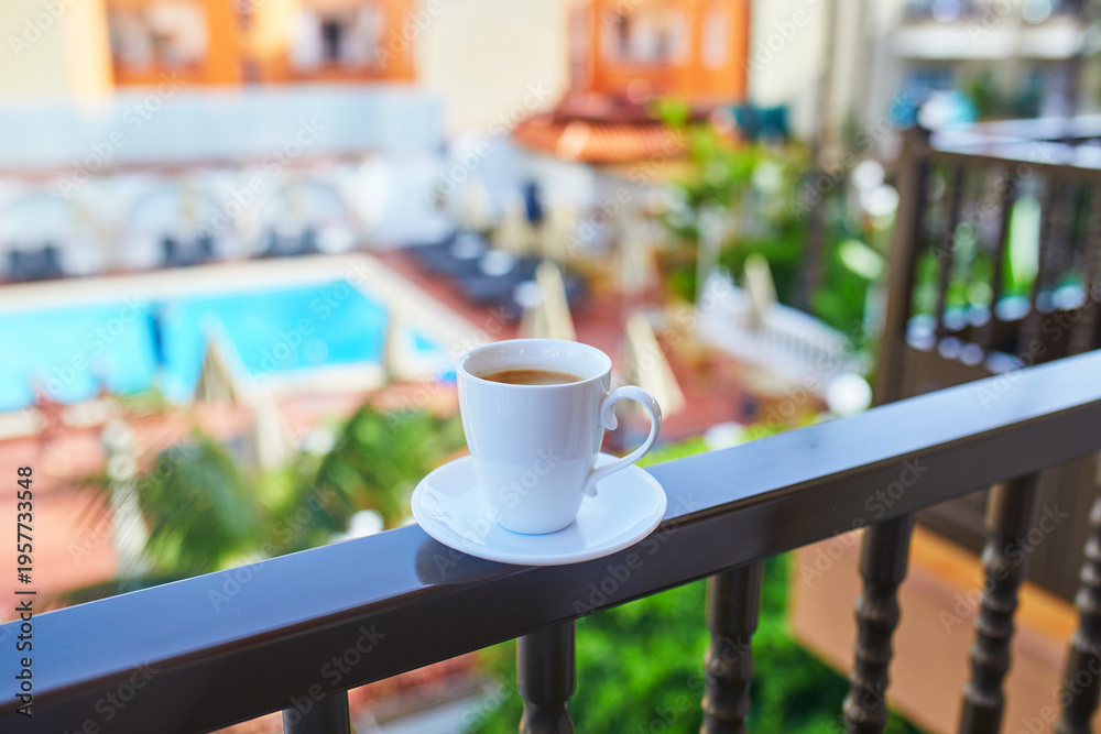 Obraz premium Cup of coffee on a hotel balcony overlooking a swimming pool and tropical courtyard in Tenerife, Canary Islands, Spain.