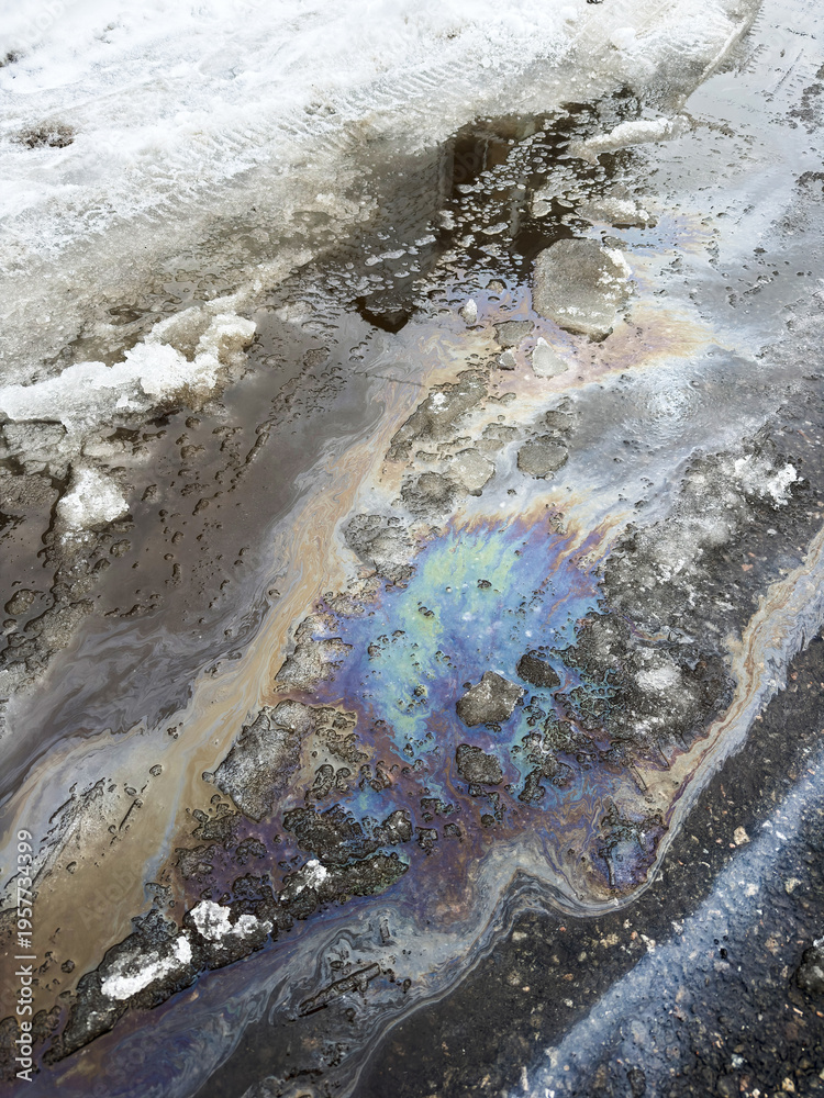 Naklejka premium La surface de la rue est recouverte d'une fine couche de pétrole et de glace. Gros plan sur une nappe de pétrole répandue au sol.