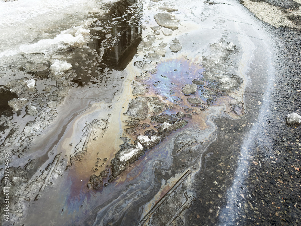 Obraz premium La surface de la rue est recouverte d'une fine couche de pétrole et de glace. Gros plan sur une nappe de pétrole répandue au sol.
