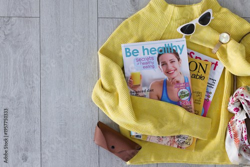 Lifestyle magazines, sweater and accessories on floor indoors, flat lay. Space for text