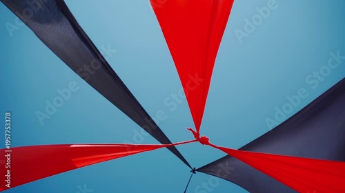 abstract view of red and black triangle shaped cloth decoration waving by wind on blue sky background. summer sea camp or beach club decoration, vibrant colors