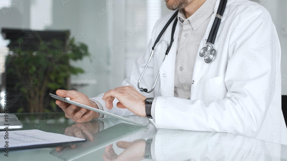 Fototapeta premium Doctor man in white coat using tablet, working with patient medical records and digital health information in clinic. Medicine, healthcare and science concept
