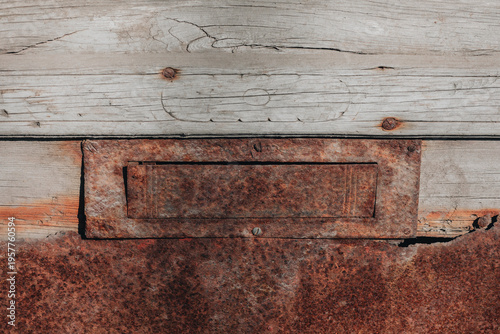 Rusty metal mail slot on weathered wooden door