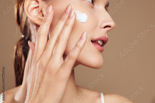 Young woman applies moisturizing cream on her clean face with fingers closeup, skin care routine, natural makeup, beauty treatment, healthy glowing complexion