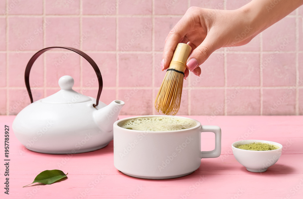 Naklejka premium Female hand holding chasen and cup of tasty matcha tea on pink wooden background
