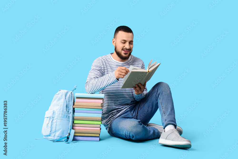 Fototapeta premium Male student with stack of books sitting on blue background