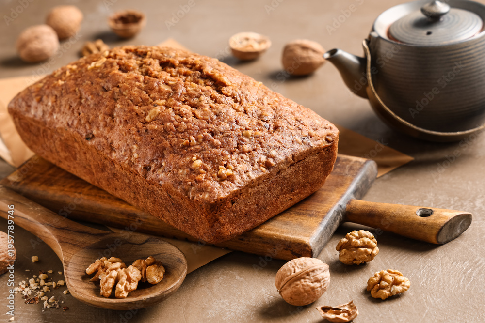 Fototapeta premium Wooden board with delicious walnut loaf cake on grey grunge background, closeup