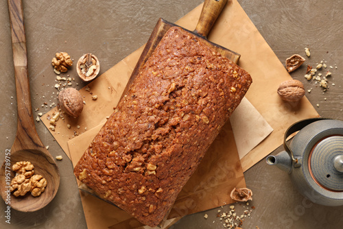 Wooden board with delicious walnut loaf cake and teapot on grey grunge background