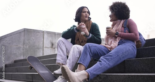 Diverse friends arriving at plaza sitting on steps with skateboard chatting over coffee catching up