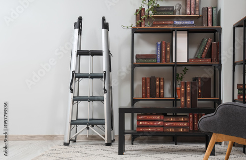 Interior of home library with bookshelves, houseplants, table and ladder near white wall