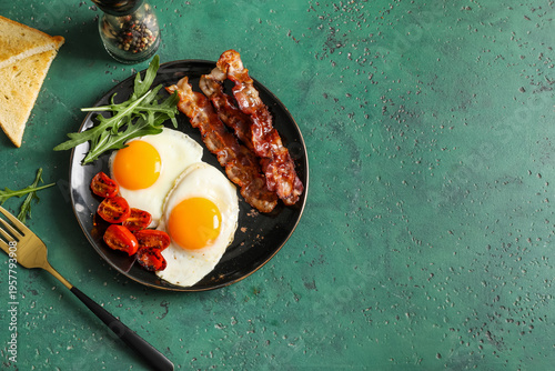 Plate with tasty fried eggs, bacon and tomatoes on green grunge background