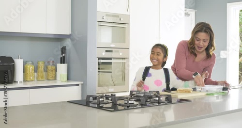 Family on kitchen island guiding daughter packing sandwich, father passing mustard, securing snack