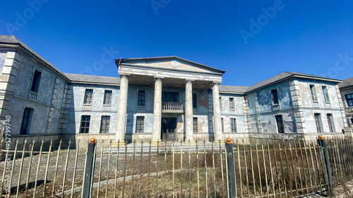 Canvas Print Historic building stands tall under blue sky at abandoned location with overgrow