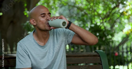 African American man sitting on bench in park, passersby causing glances, drinking to quench thirst