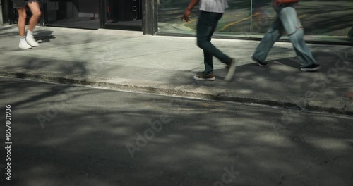 Diverse pedestrians entering from left, walking across sidewalk by reflective glass, heading onward