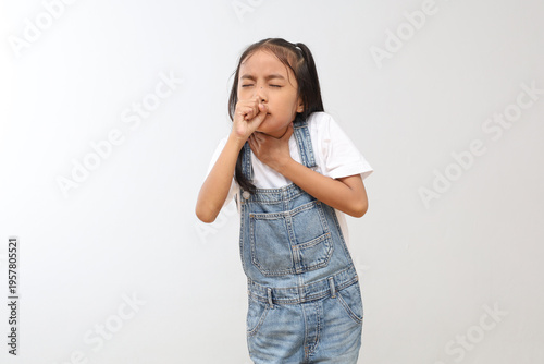 A small child isolated on a gray background, making a coughing gesture while covering his mouth.