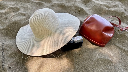 Travel accessories including camera, hat and leather bag on sandy beach. Vacation and summer holiday concept