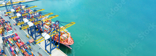 Aerial view of container port with colorful cranes loading cargo ship beside turquoise sea during daytime, showcasing global logistics, shipping industry efficiency and international trade network.