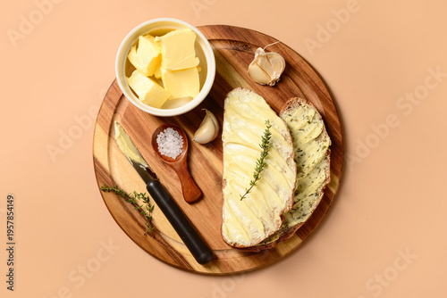 Wooden board of bread slices with fresh butter, garlic and salt on brown background