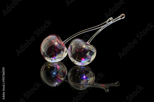 A pair of cherries carved entirely from clear glass, from a fine glass, are placed on a glossy black surface. Light passes through the cherries, creating a colorful light scattering reflection around 