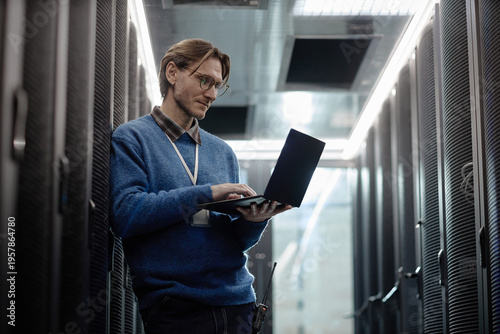 Obraz na plátně Caucasian middle aged man standing in server room working on laptop, wearing gla