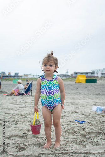 little girl playing on the beach with a bucket in hand