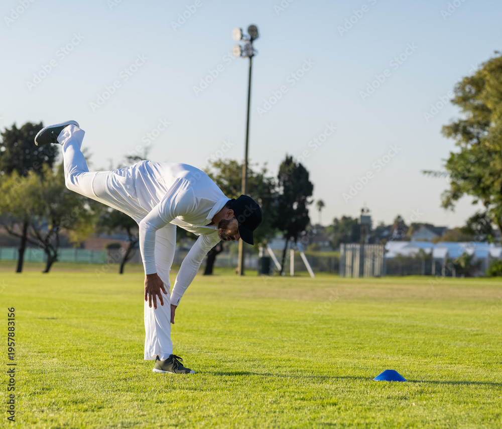 Obraz premium Mid-adult man balancing on sports field wearing white kit, black cap, gray shoes, blue cone nearby