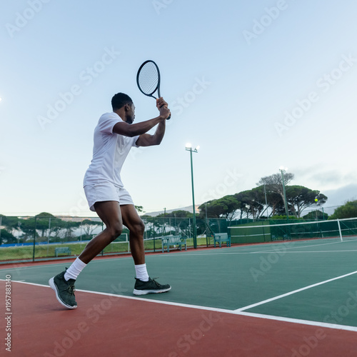 Valokuva African American man in white holding racket preparing swing near net with tenni