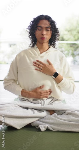 Vertical video: After placing hands on torso, non-binary yogi breathing deeply on mat near window