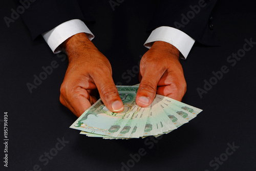 Tableau sur toile Hands holding UAE currency notes closeup shot against black background, Payment
