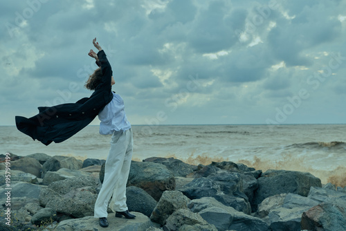Slika na platnu Dynamic figure on a rocky shore with cape billowing, facing the open sea, convey