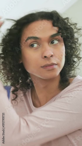 Vertical video: Bringing hand to face, non-binary adult grooming in bedroom in pink top with rings