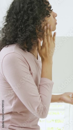 Vertical video: Dabbing pink top person applying cream at vanity seeing dab in mirror, blending