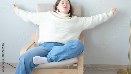A young woman in a white sweater sits on chair and stretches, relaxation concept.